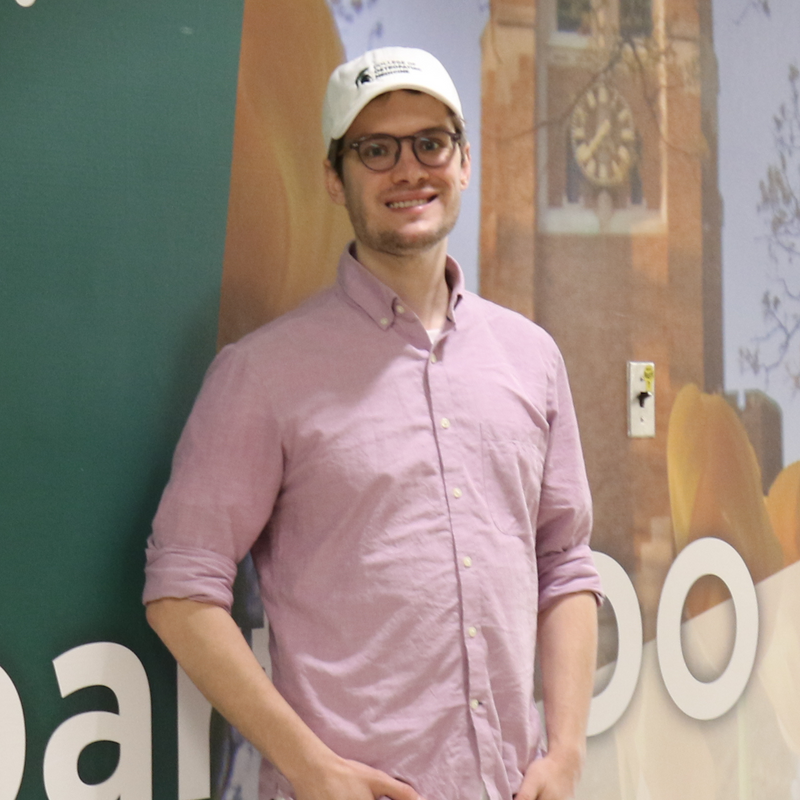 Man wearing a pink shirt and white MSU Osteopathic Medicine cap