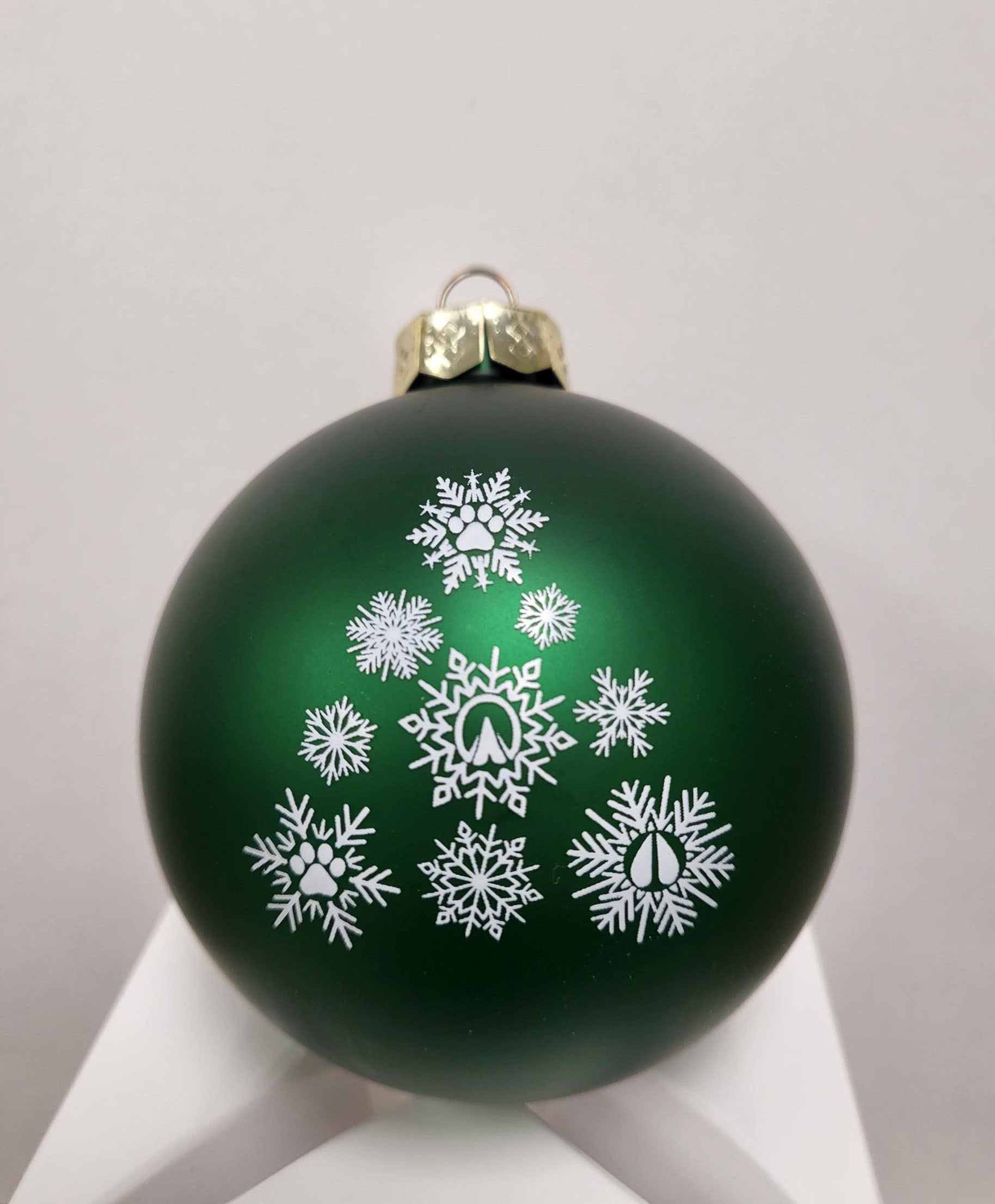 Green ornament with a gold tone top, white snowflakes with different animal prints in center. 