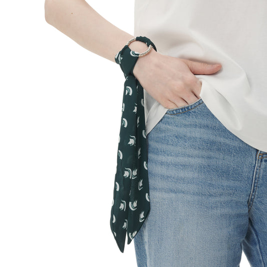 Model wearing a dark green Michigan State scarf with repeating white Spartan helmet logos, styled around the wrist with a silver-tone ring detail.