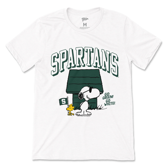 White Michigan State Spartans T-shirt featuring large arched “SPARTANS” lettering above a Snoopy and Woodstock graphic in front of a green doghouse. The design includes a green Michigan State flag with the Spartan helmet logo and the phrase “GO GREEN! GO WHITE!” printed on the front. Short-sleeve crewneck style.