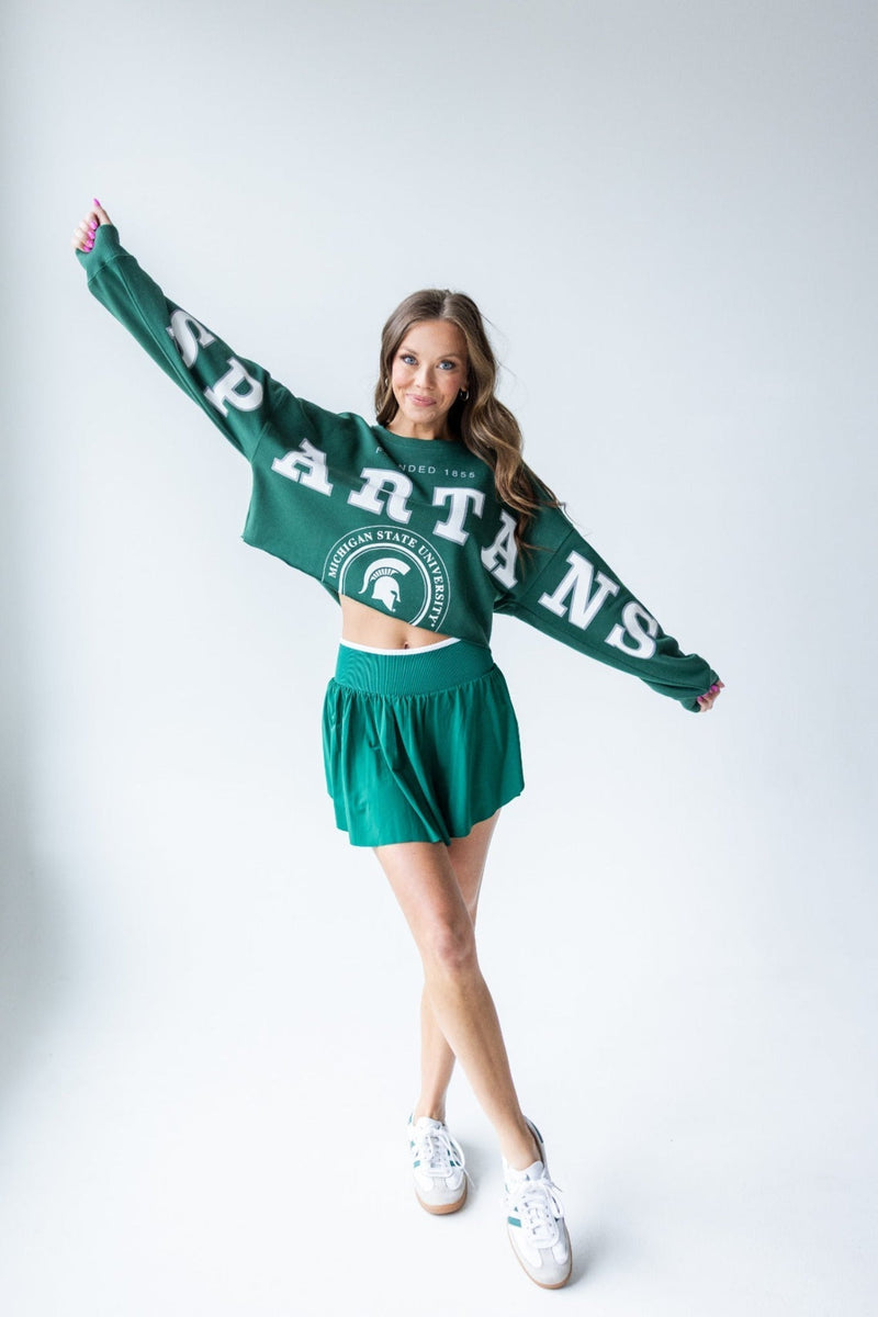 Green cropped sweatshirt with 'SPARTANS' in large white letters across the chest and sleeves, featuring a circular 'MICHIGAN STATE UNIVERSITY' logo with a Spartan helmet.