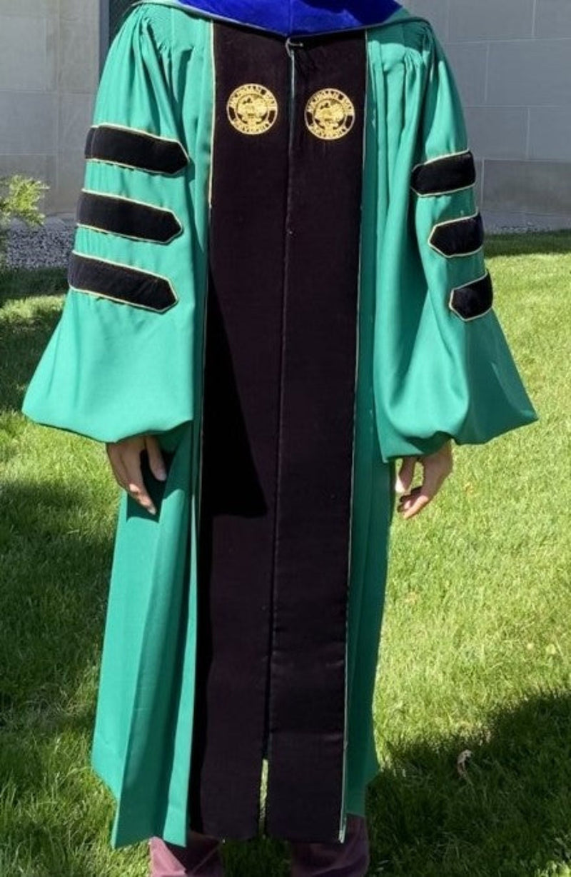 A person wearing a Madison Doctoral Green Gown with velvet panels and bell sleeves, featuring a zipper closure and a pocket slit.