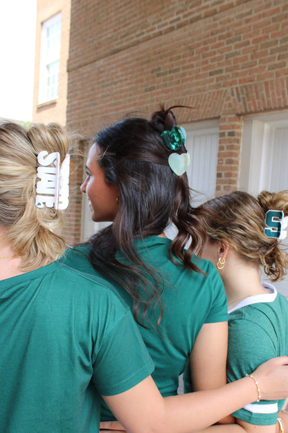 Three women standing together each wearing a MSU themed hair clip. 