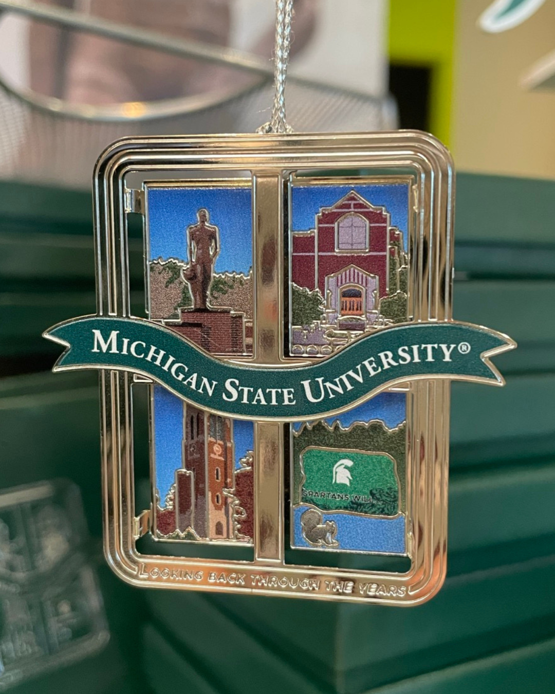 Decorative ornament featuring Michigan State University landmarks split into four window panes, including the Union, the Spartan statue, Beaumont Tower. and the Rock, with a ribbon banner reading 'Michigan State University.'