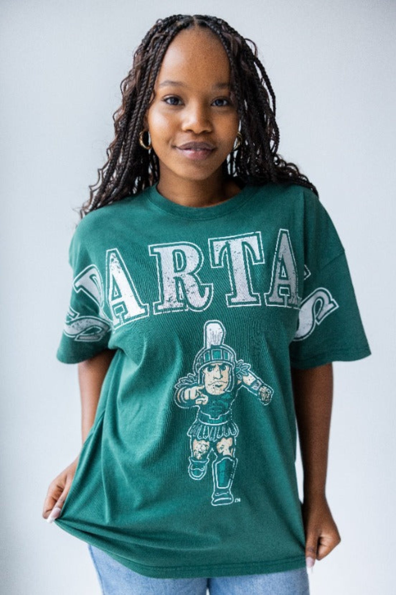 Green t-shirt featuring the word 'SPARTA' in bold white letters across the chest, with an illustration of a Spartan warrior holding a shield and spear below the text.
