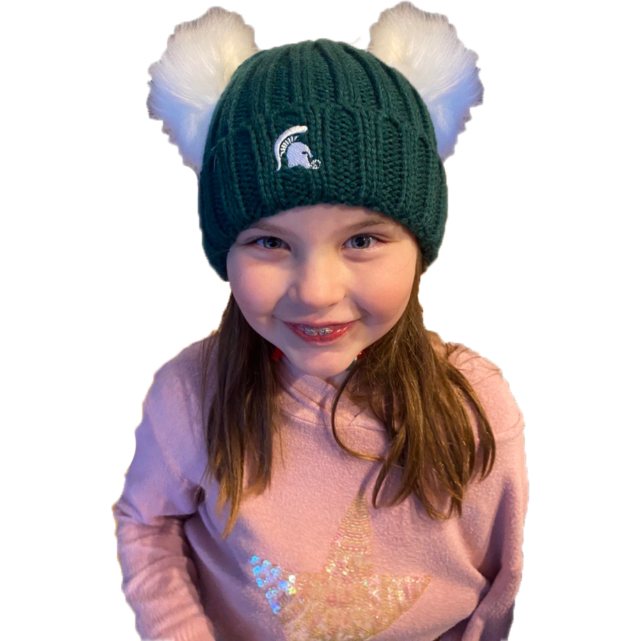 A girl wearing a green beanie with two white pom knits. The Spartan Helmet logo is embroidered on the front of the beanie in white. 