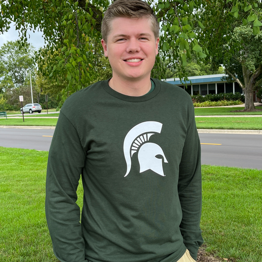 A man wearing a dark green crewneck, long-sleeve t-shirt. Across the center chest is a large white Spartan Helmet logo.