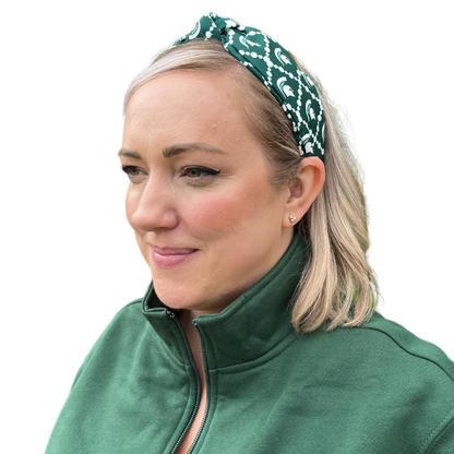 A person with blonde, shoulder-length hair wearing a green and white headband with sublimated Spartan Helmet logos and white dots linked in diamond shapes around the helmets.