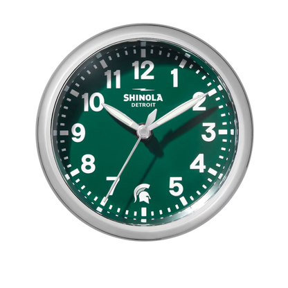 Close up of the Shinola desk clock with a green face, wooden base, and silver rim. The numbers are white and there is a white Spartan Helmet logo in place of the number 6.