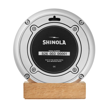Shinola desk clock case back on a wooden stand.
