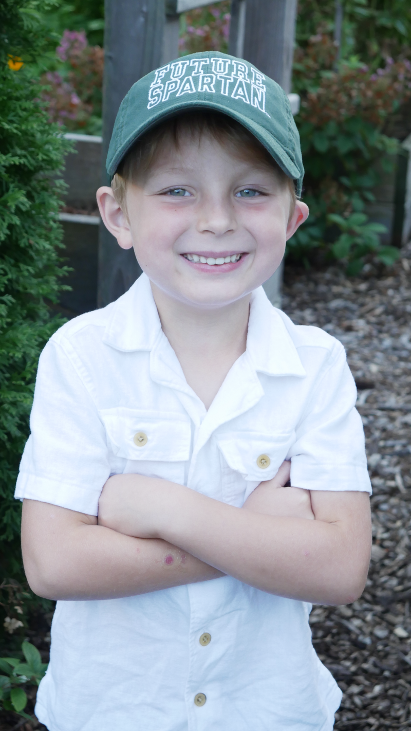 Young boy wearing a green 'Future Spartan' cap and white shirt.