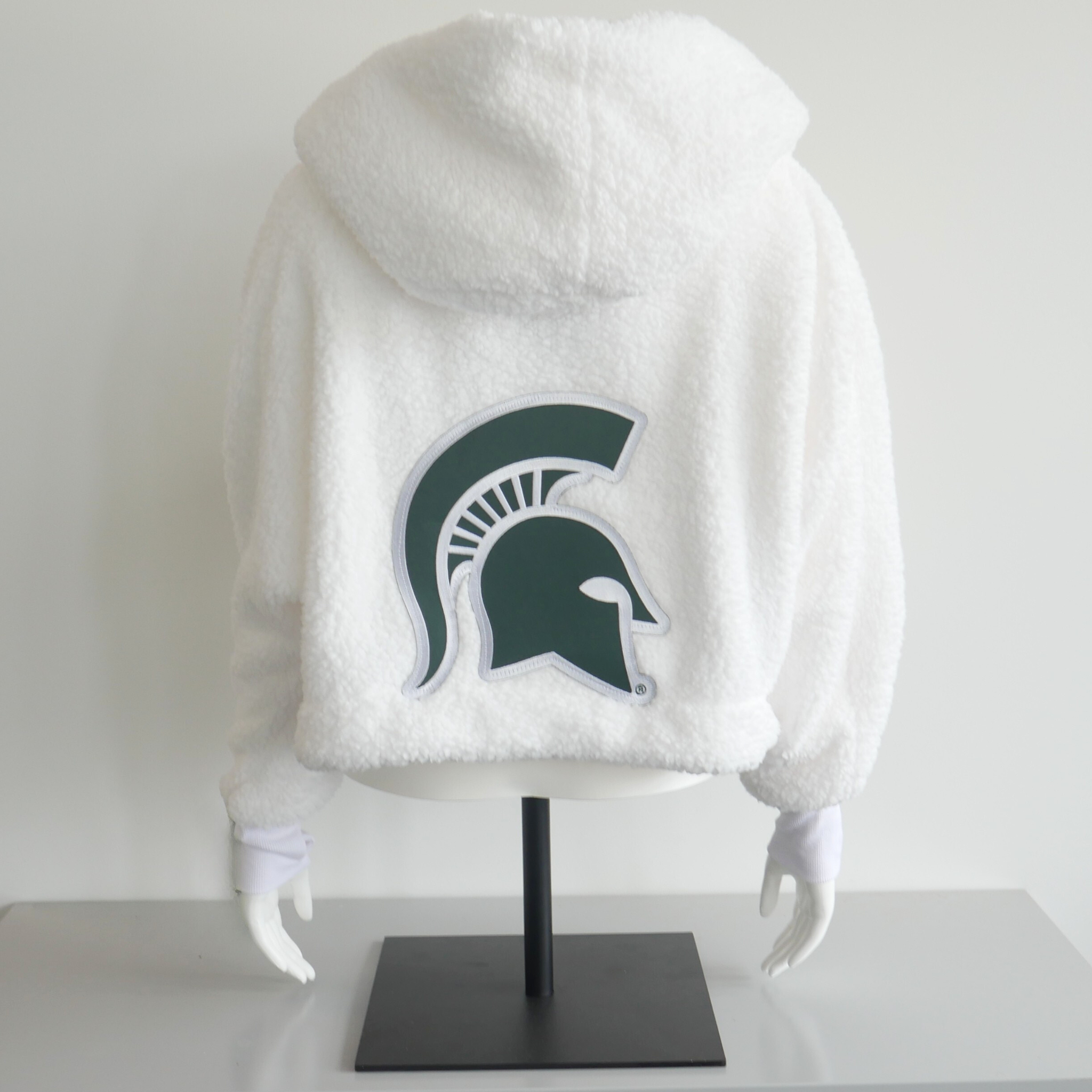 A white lounge jacket on a mannequin. On the back of the lounge jacket is a large green Spartan helmet logo patch. 