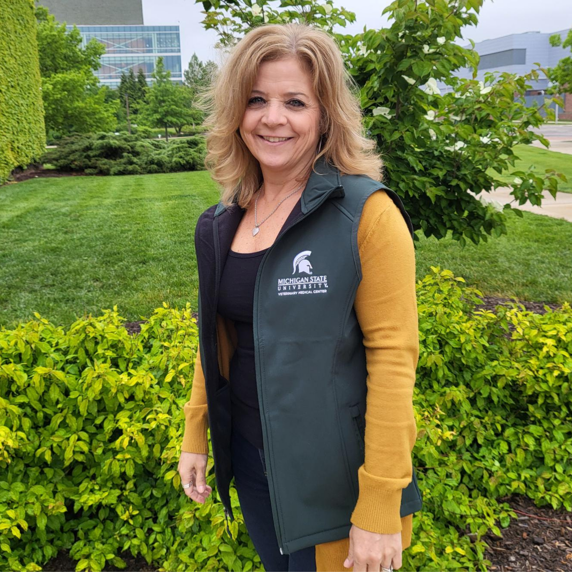 Person showing the left side of a green zippered vest with a white embroidered College of Osteopathic Medicine logo on the left upper chest. 