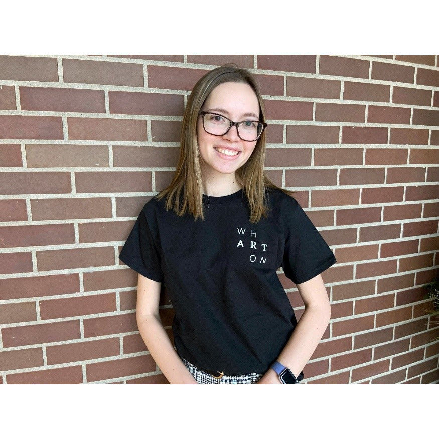 Female student wearing black Wharton Center T-shirt in front of a brick wall.