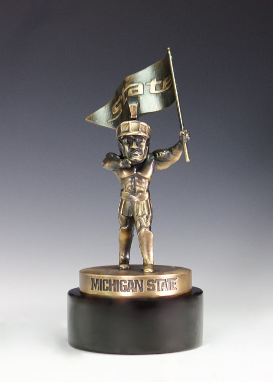 A bronze Sparty statue holding a pennant flag with the word "State" on a black base.