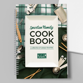 Cover of the The Spartan Family Cookbook. The text on the cover is shown on a plate on top of green and white tablecloths with kitchen utensils placed around. 
