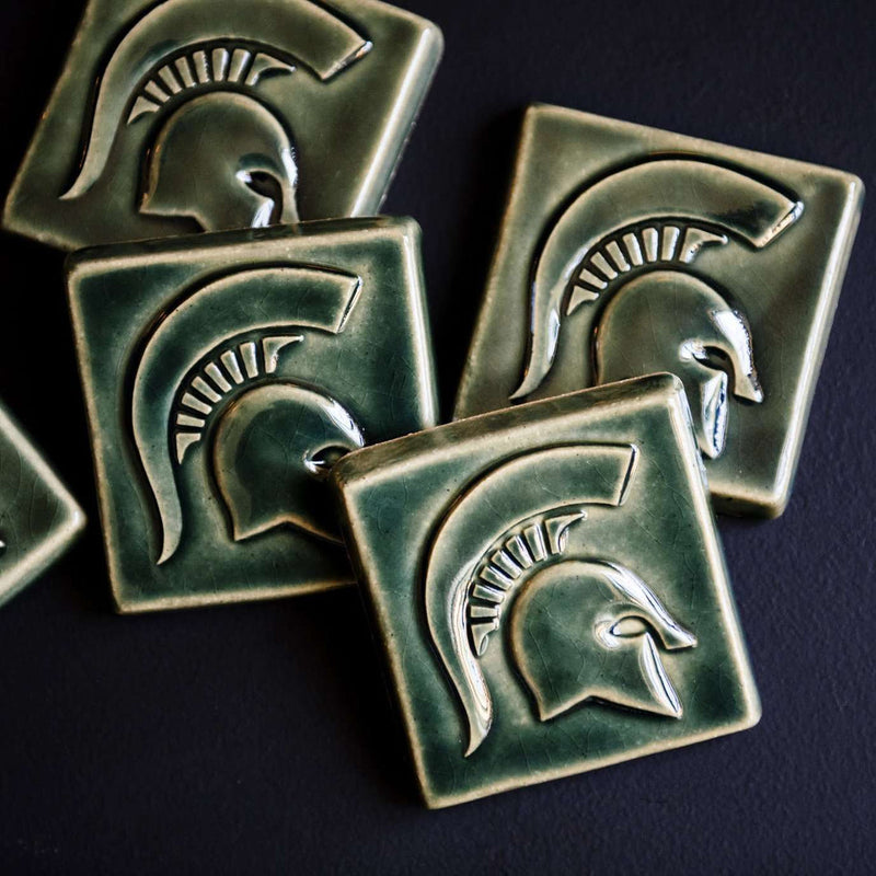 Green ceramic tiles with Spartan helmet design on a dark background