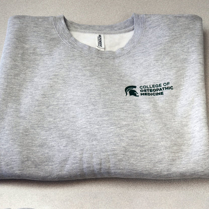 Front of heather gray crewneck sweatshirt with College of Osteopathic Medicine logo printed in forest green on the left upper chest. 