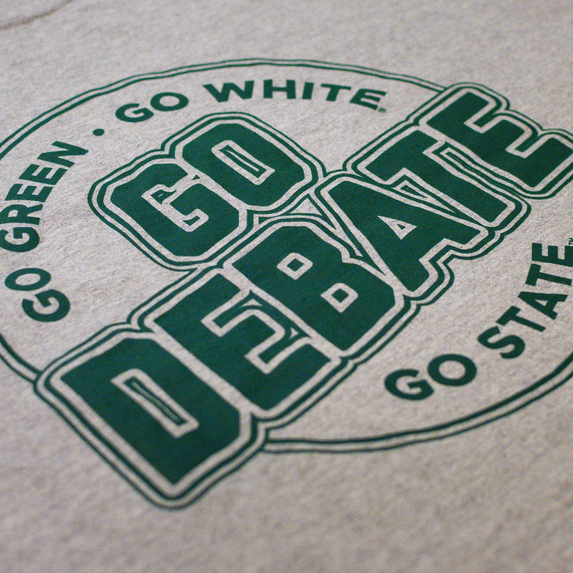 Close-up of a heather gray t-shirt featuring a green printed graphic that reads 'GO DEBATE' with 'GO GREEN . GO WHITE' and 'GO STATE' surrounding it.