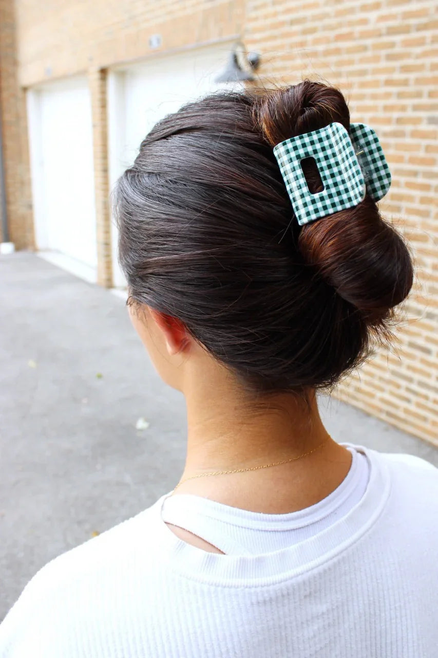 Person with a bun hairstyle with a green and white gingham hair clip outdoors.