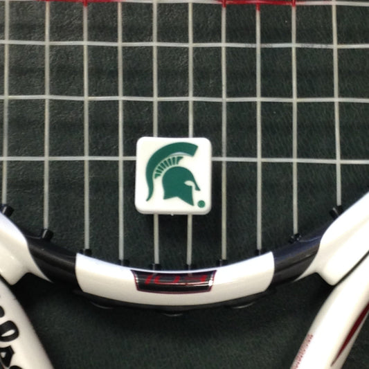 A white tennis racket dampener with a green Spartan Helmet logo placed on a tennis racket.